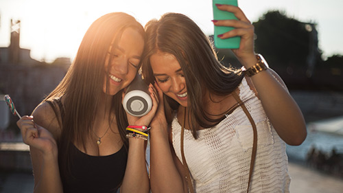 Duas raparigas a ouvir música com coluna bluetooth emparelhada com telemóvel